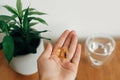 Dietary supplements. Hand holding omega 3 two capsules above wooden table with glass of water. Morning dose of vitamin. Fish oil