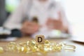 Dietician doctor and pile of vitamin D capsules with D symbol on wooden cube.