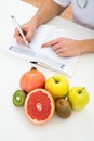 Dietician writing prescription with fruits on desk