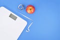 Dieting concept with scale, measuring tape and apple on blue background Royalty Free Stock Photo