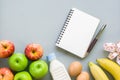 Dieting, healthy and active lifestyles Concept, apples, bananas, egges, tape measure, bottle of milk, blank notebook on grey back