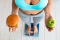 Woman Choosing Between Hamburger And Apple Standing On Weight-Scales, Cropped