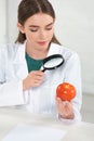 Dietitian in white coat looking at tomato through magnifying