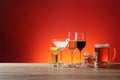 Different alcohol drinks on wooden table against red background. Space for text