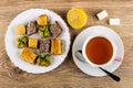 Different baklava in plate, lemon, sugar, cup with tea, spoon on saucer on table. Top view