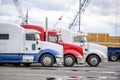 Different big rig semi trucks standing in row on industrial parking lot with cranes waiting for loads for next route Royalty Free Stock Photo