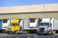 Different big rigs semi trucks with refrigerator semi trailer standing on the warehouse dock gates loading cargo for the next Royalty Free Stock Photo