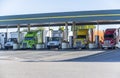 Different big rigs semi trucks standing on fuel station for truck refueling and continuation of the route