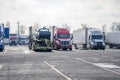 Different big rigs semi trucks with different semi trailers with cargo standing in row on truck stop