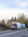 Different big rigs semi trucks with semi trailers standing out of service on the highway road shoulder