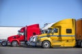 Different big rigs semi trucks with semi trailers standing in row on truck stop parking lot for truck drivers rest and adherence