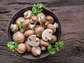 Different brown colored edible mushrooms in the wooden bowl on wooden table with herbs. Top view