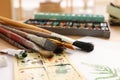 Different brushes, colorful paints, palette and drawing on table indoors, closeup. Artist`s workplace