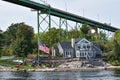 Different buildings in a grassy area on the coast of a lake during daytime, and surrounded by trees. United States flag, and boat