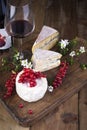 Different cheese with white and blue mold. A glass of red wine and fresh red currant berries. White flowers. Wooden background and Royalty Free Stock Photo