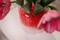 Different color fillers and tulips in glass vase, closeup. Water beads