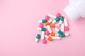 Different colorful drugs falling from the white  bottle on pink background. Royalty Free Stock Photo