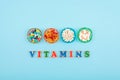 Different colorful pills and capsules in round plate and multicolored word VITAMINS on blue background. Nutrition supplement, drug