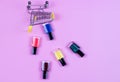 Different colors nail polishes and a shopping trolley on a pink background