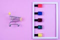 Different colors nail polishes and a shopping trolley on a pink background