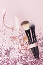 Different Cosmetic makeup brushes with pink ribbon and holographic glitter confetti in the form of stars on pink background Flat Royalty Free Stock Photo