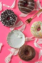 Different donuts coated with chocolate frosting on a pink background with petals of peony, vintage saucer and fork.