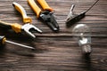 Different electrician's tools with lamp bulb on wooden background