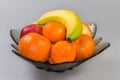 Different fruits in glass bowl on gray surface, side view