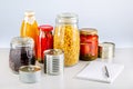 Different glass jars with grains, pickled vegetables, pasta, cans of canned food. Groceries with list on the table.