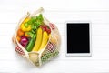 Different health food - yellow bell pepper, tomatoes, bananas, lettuce, green, cucumber, onions in mesh bag tablet with black touc Royalty Free Stock Photo