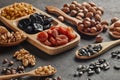 Different kinds of nuts, dried fruits in wooden spoones and dish on black slate background. Healthy food. Vegetarian nutrition