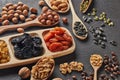 Different kinds of nuts, dried fruits in wooden spoones and dish on black slate background. Top view. Healthy food. Vegetarian