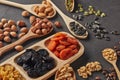 Different kinds of nuts, dried fruits in wooden spoones and dish on black slate background. Top view. Healthy food. Vegetarian