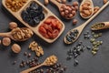 Different kinds of nuts, dried fruits in wooden spoones and dish on black slate background. Top view. Healthy food. Vegetarian