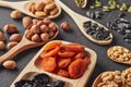 Different kinds of nuts, dried fruits in wooden spoones and dish on black slate background. Top view. Healthy food. Vegetarian