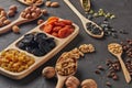 Different kinds of nuts, dried fruits in wooden spoones and dish on black slate background. Top view. Healthy food. Vegetarian