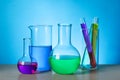 Different laboratory glassware with colorful liquids on wooden table against light blue background Royalty Free Stock Photo