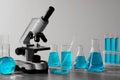 Different laboratory glassware with light blue liquid and microscope on table Royalty Free Stock Photo