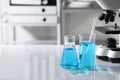 Different laboratory glassware with light blue liquid near microscope on table, space for text Royalty Free Stock Photo