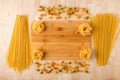Different macaroni are laid out on a bamboo cutting Board and a wooden background