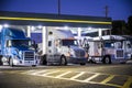 Different make and models big rig semi trucks with semi trailers standing on the truck stop parking lot under the lighted shelter Royalty Free Stock Photo