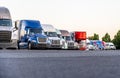 Different Big rigs semi trucks standing in row on truck stop parking lot for rest and comply with the movement schedule