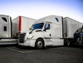 White big rig semi truck with semi trailer standing in row with another semi trucks on the night truck stop parking lot for rest Royalty Free Stock Photo