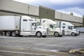 Different models of big rigs semi trucks with dry van semi trailers loading cargo at warehouse docks with rain weather Royalty Free Stock Photo