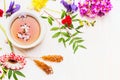 Different multicolored flowers lined up around cup of tea, sugar sticks, top view