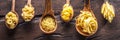 Different pasta types in wooden spoons on the table. Top view