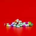 Different pharmaceutical medicine pills, tablets and capsules in different colors on red background. Health care concept. 3D Royalty Free Stock Photo