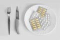 Different pills on a plate with cutlery. Means for suppressing appetite