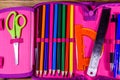 Different school stationeries pens, pencils, ruler, protractor and scissors in a pink pencil box. Top view