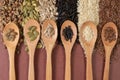 Different seeds -quinoa, pumpkin, coffee, pepper, rice, sunflower- in wooden spoons on a surface of different seeds and brown Royalty Free Stock Photo